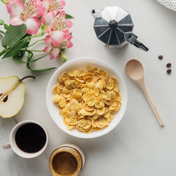 top view of bowl of corn flakes with coffee and flowers bouquet on white