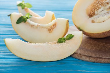 close-up view of sliced sweet ripe melon with mint on blue wooden surface clipart