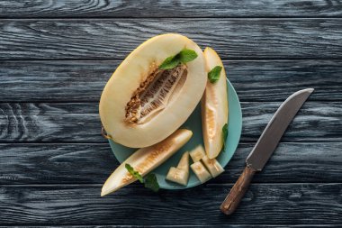 top view of sweet ripe sliced melon with mint on plate and knife on wooden surface  clipart