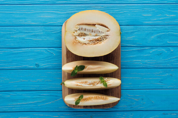 top view of sweet ripe sliced melon on cutting board on blue wooden surface 