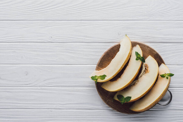 top view of sweet ripe sliced melon with mint in round wooden board on table