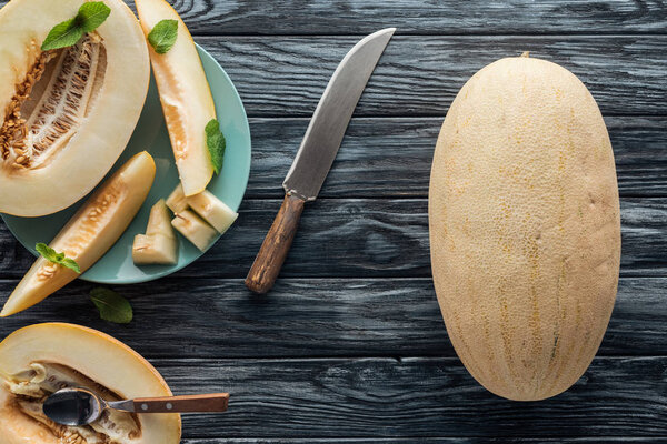 top view of sweet ripe melons, spoon and knife on wooden surface