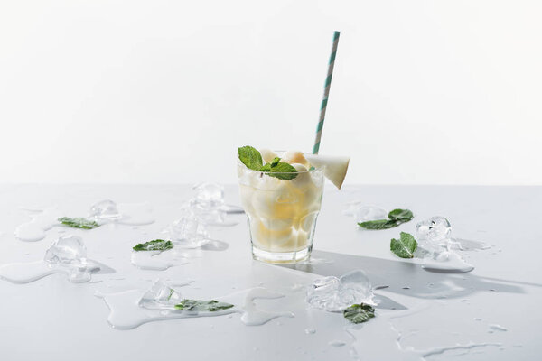 delicious summer drink with mint and melon in glass and melted ice cubes on white 