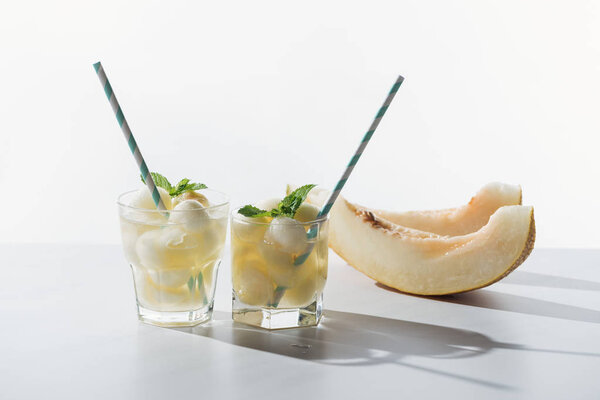 slices of sweet honeydew melon and refreshing beverage with melon and mint in glasses on white
