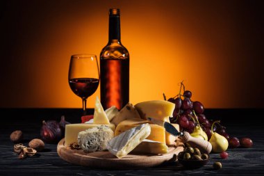 different types of cheeses and alcohol drink on table on orange clipart
