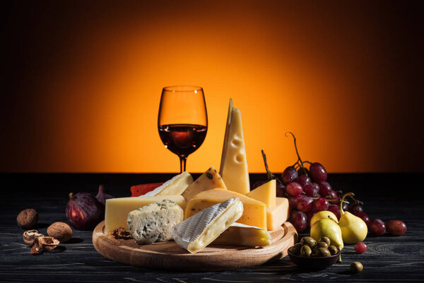 different types of cheeses, wineglass and fruits on table on orange