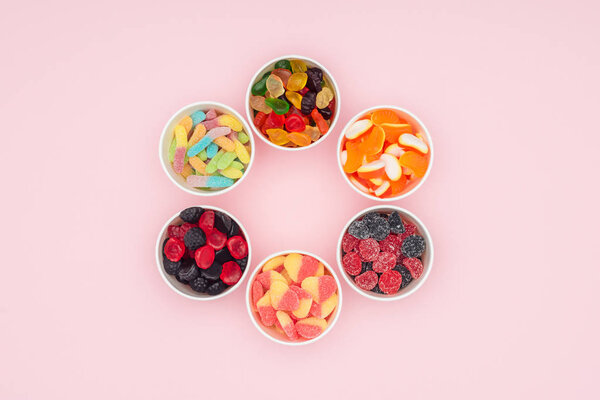 top view of paper cups with yummy jelly candies in circle isolated on pink