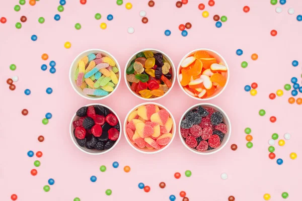 高视图的纸杯与美味的果冻糖果和分散糖衣杏仁下落在粉红色的孤立 — 图库照片