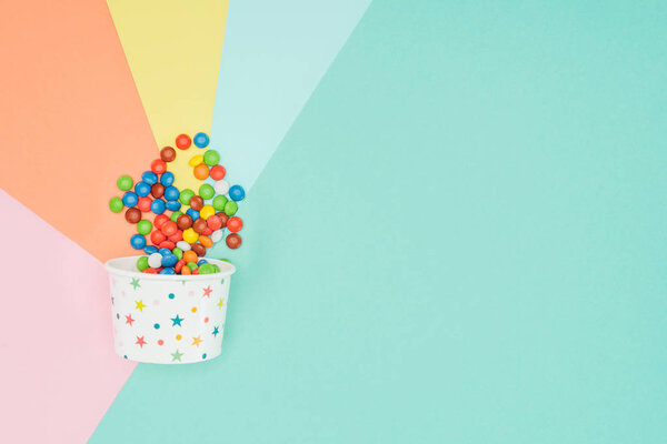 top view of appetizing dragee candies in paper container on colored surface