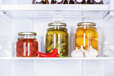 preserved vegetables in glass jars and ripe chili peppers in fridge clipart