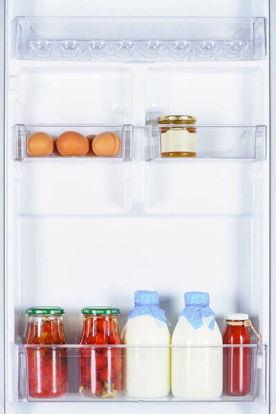 eggs, preserved tomatoes and bottles of milk in fridge