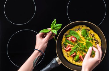 Kırpılan atış kadının siyah soba üzerinde tavada omlet pişirme