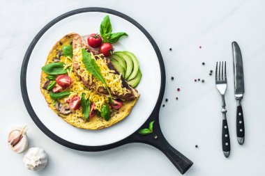 food composition with healthy omelette on wooden board and cutlery on white marble tabletop clipart