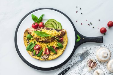 Ahşap tahta üzerinde sağlıklı omlet ve beyaz mermer masa üzerinde çatalı gıda kompozisyonu