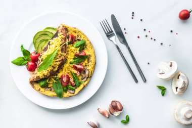 flat lay with homemade omelette with cherry tomatoes, avocado pieces, spinach and cutlery on white marble surface clipart