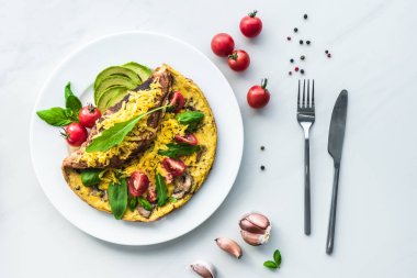 kiraz domates, avokado parçaları ve çatal bıçak takımı ile ev yapımı omlet üstten görünüm beyaz mermer yüzeyi