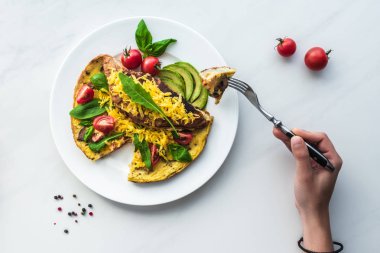 kadının kahvaltıda ev yapımı omlet ile masa üstü, elinde çatal ile kısmi görünümü
