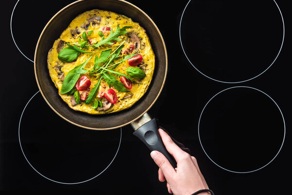 cropped shot of woman cooking omelette in frying pan on black stove