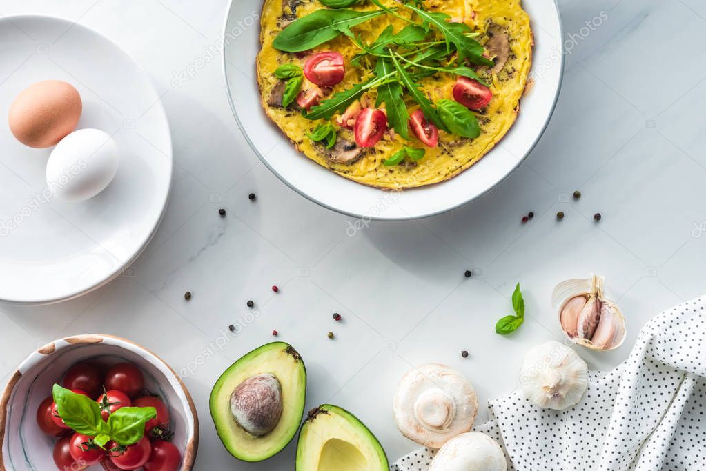 flat lay with cooked omelette for breakfast and ingredients arranged on white marble surface