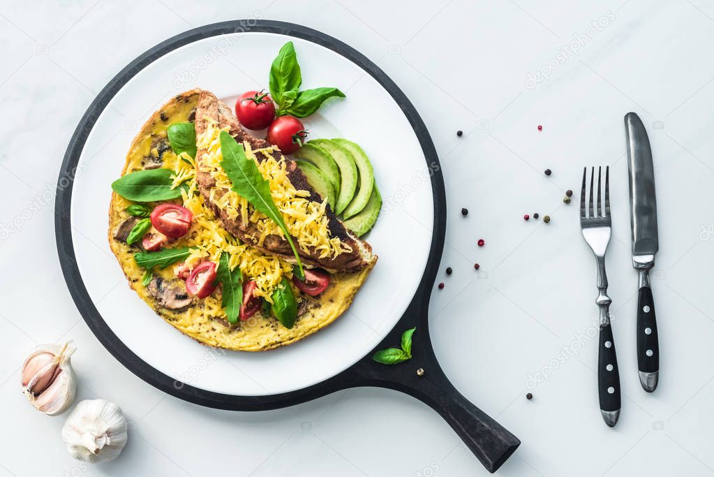 food composition with healthy omelette on wooden board and cutlery on white marble tabletop