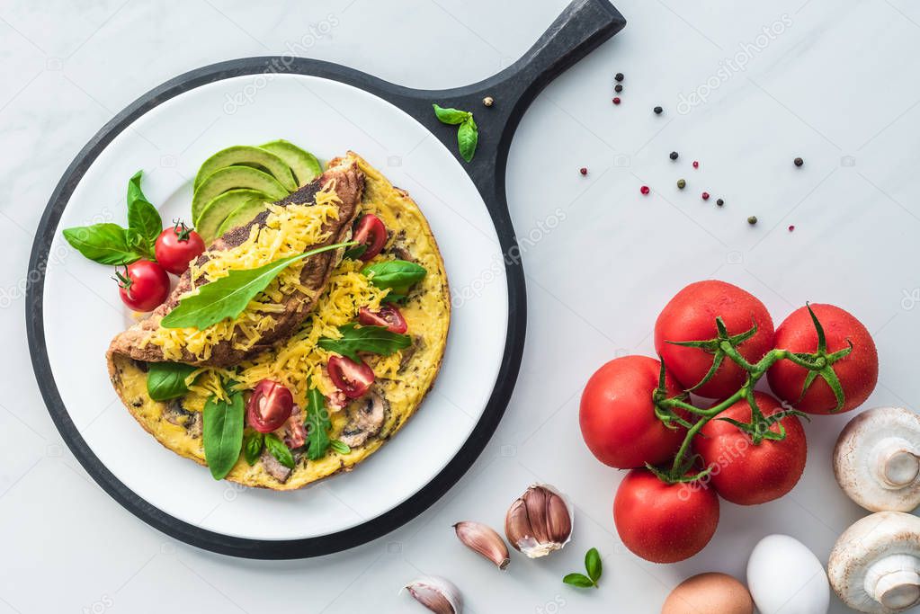 food composition with healthy omelette on wooden board and ingredients on white marble tabletop