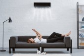 uvolněná mladá žena pomocí smartphone na gauči pod klimatizaci visí na zdi