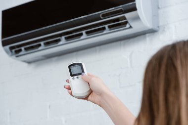 cropped shot of woman pointing at air conditioner with remote control