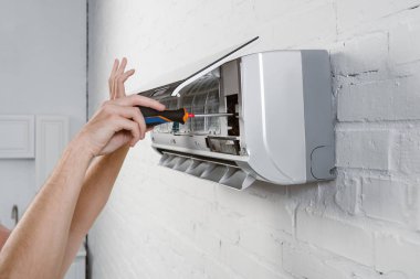 cropped shot of repairman taking off filter from conditioner with screwdriver clipart