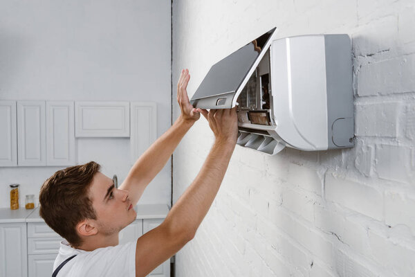 repairman taking off dirty filter from air conditioner hanging on white brick wall