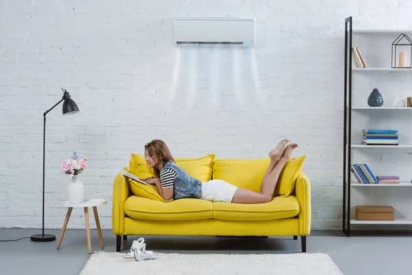 Attractive Young Woman Reading Book Couch Air Conditioner Hanging Wall — Stock Photo, Image