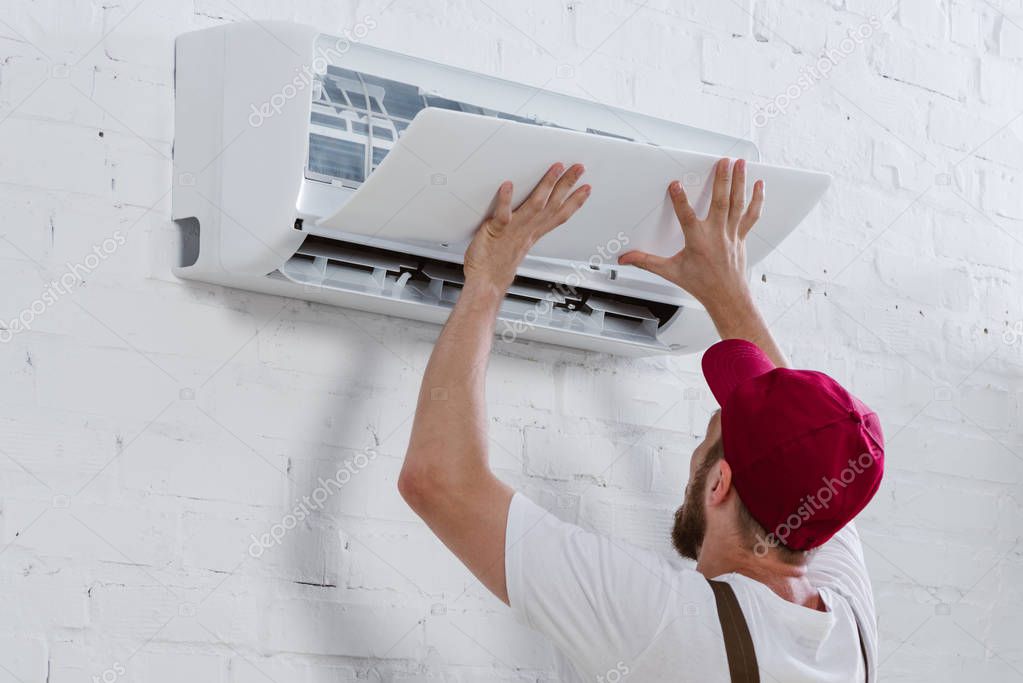 Close-up shot of young repairman fixing air conditioner hanging on white brick wall