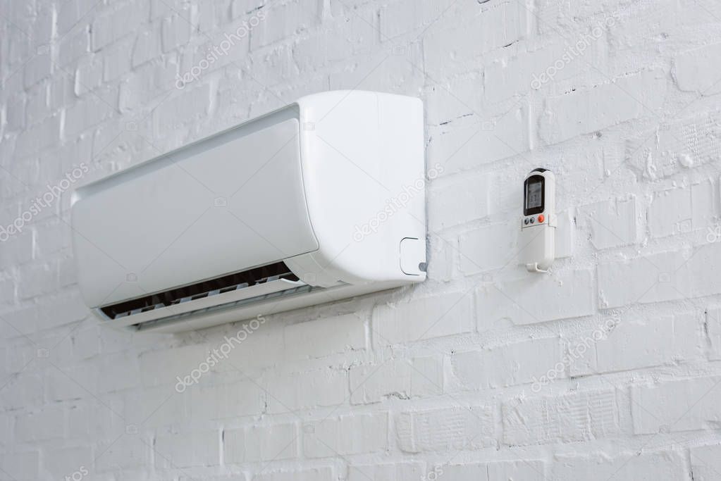Air conditioner hanging on white brick wall with remote control
