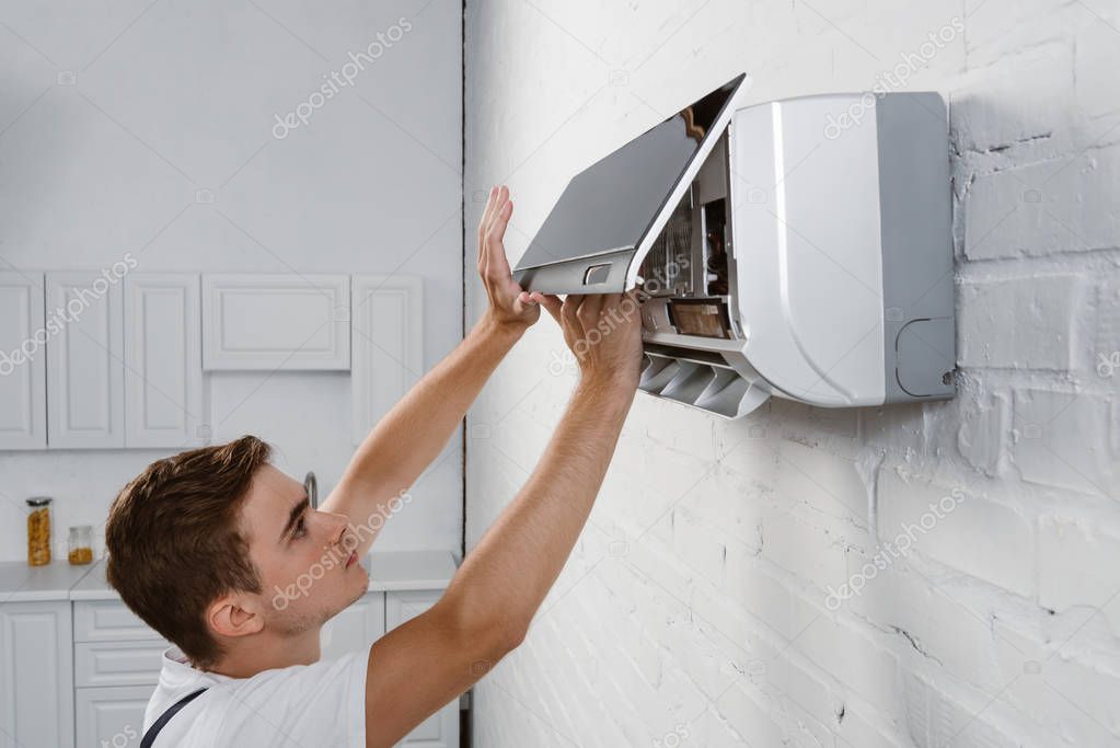 Repairman taking off dirty filter from air conditioner hanging on white brick wall