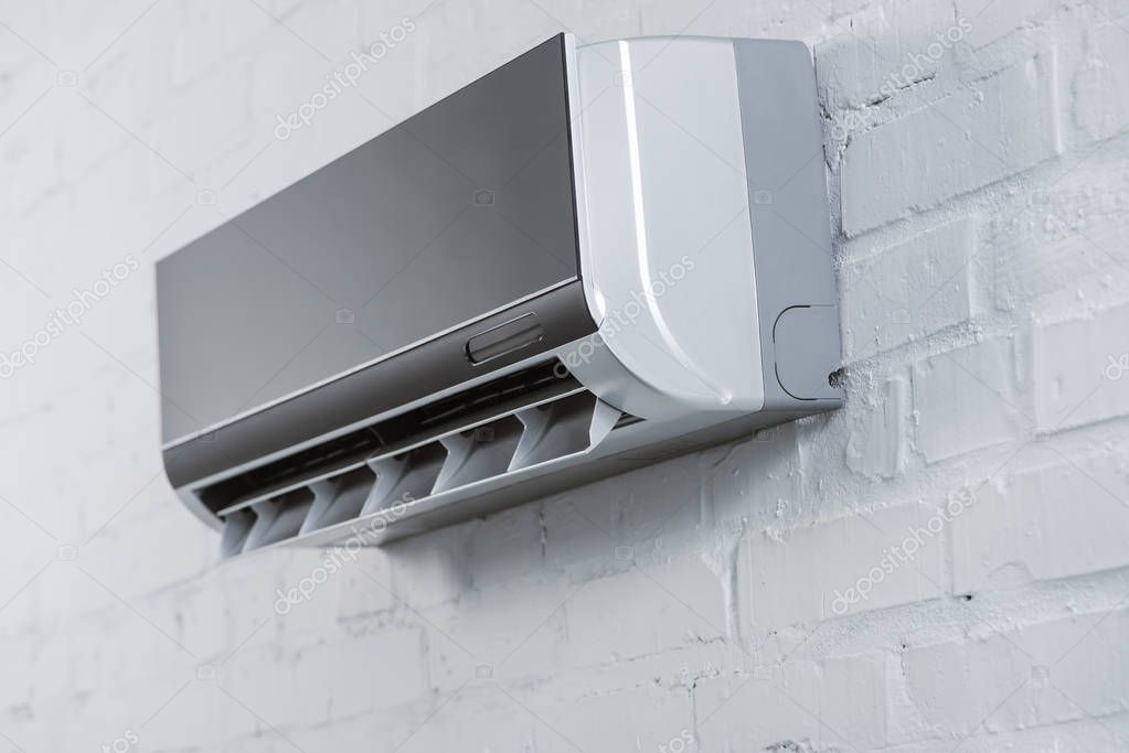 Close-up shot of modern air conditioner hanging on white brick wall