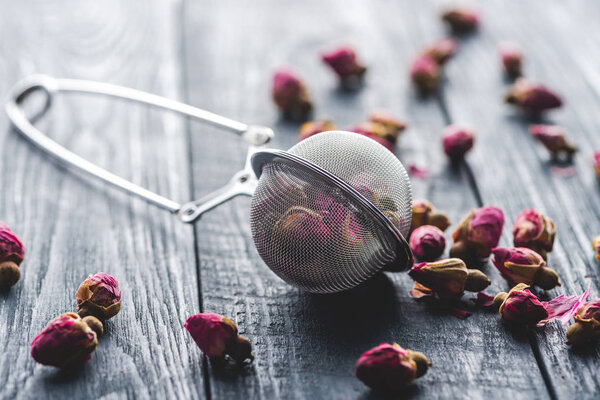 dried rose buds tea and tea strainer on wooden table