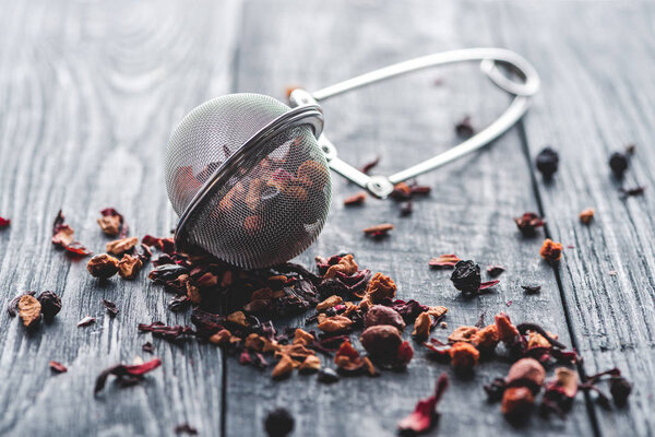 tasty black tea with dried fruits and tea strainer on wooden table