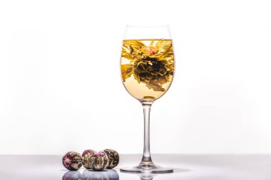 glass of tasty chinese flowering tea with tea balls on reflecting table clipart