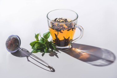 cup of black tea, mint and tea strainer on white tabletop  clipart