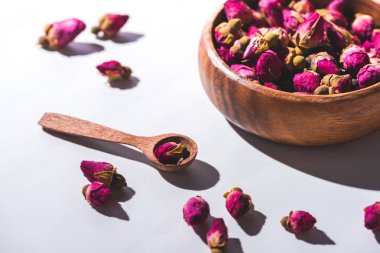dried rose buds in wooden bowl and spoon on white tabletop 