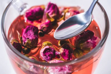 close up of tea with dried pink rose buds and spoon