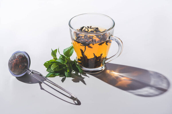 cup of black tea, mint and tea strainer on white tabletop 