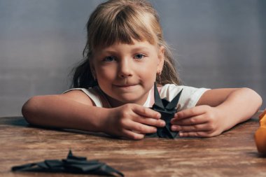 portrait of little child with black paper bats looking at camera at home clipart