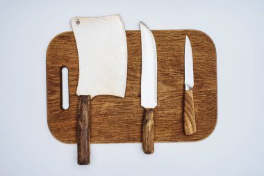 top view of different kitchen knives on wooden chopping board isolated on grey   clipart