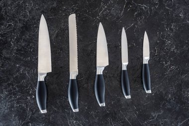 top view of different kitchen knives arranged on black marble surface   clipart