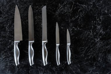 top view of different kitchen knives arranged on black marble surface with copy space  clipart