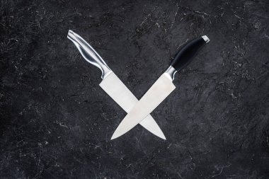 top view of two kitchen knives arranged on black surface  clipart