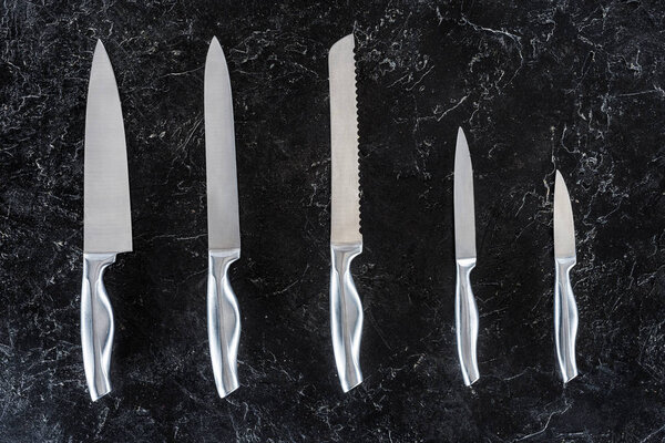 top view of different kitchen knives arranged on black surface 