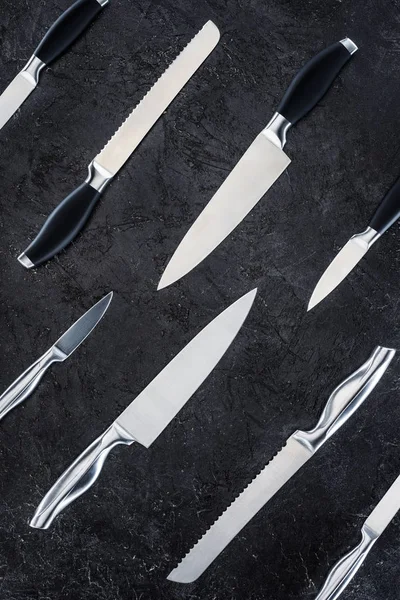 top view of various kitchen knives arranged on black surface, seamless pattern