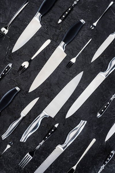 top view of various forks and knives on black surface
