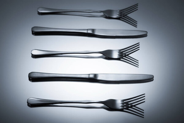 shiny stainless steel forks and knives reflected on grey    